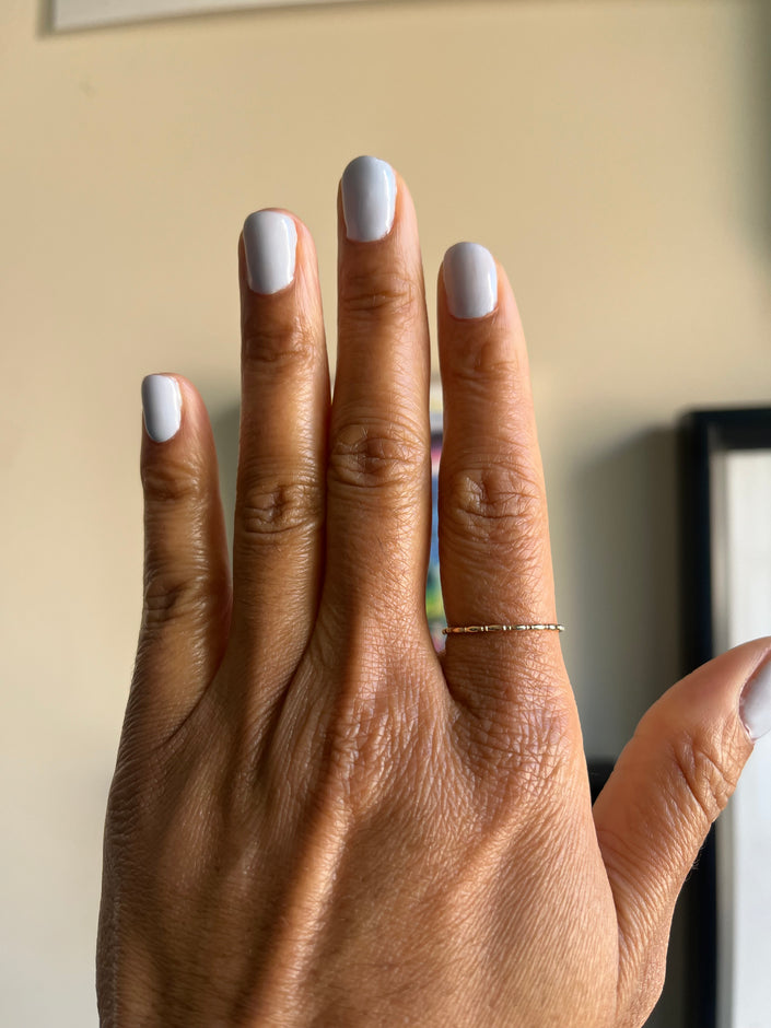 Hand with light gray nail polish and a gold ring on a neutral background