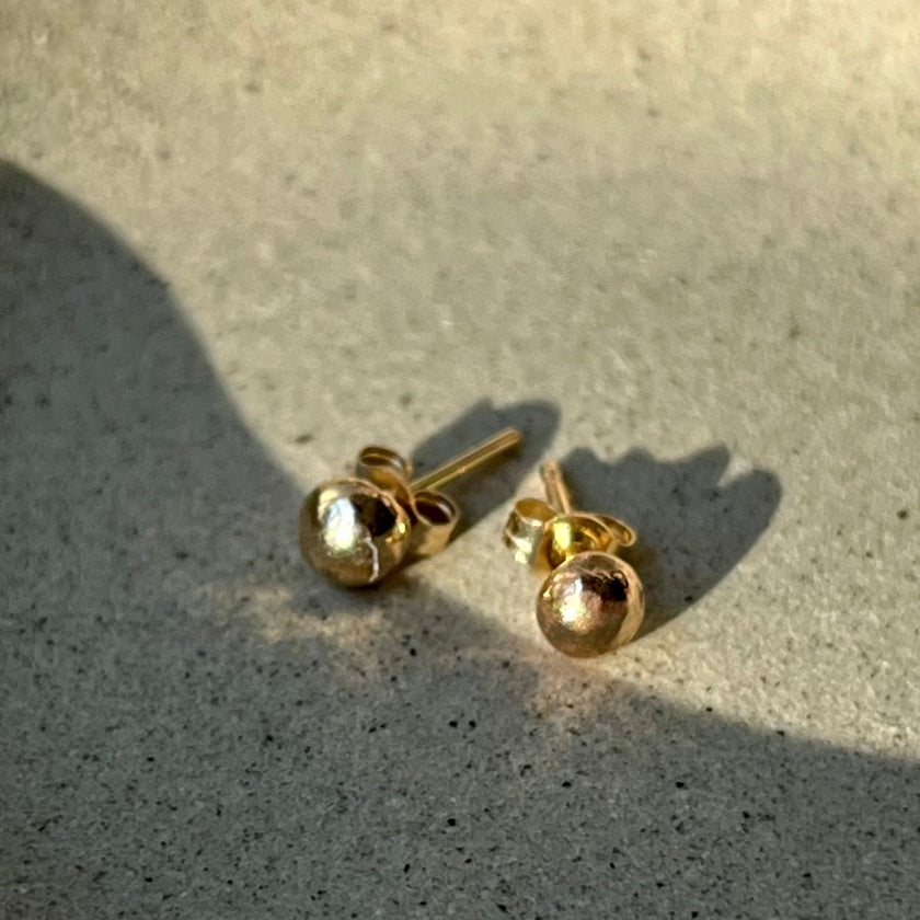 Close-up of recycled 14kt solid gold pebble studs showing polished organic texture